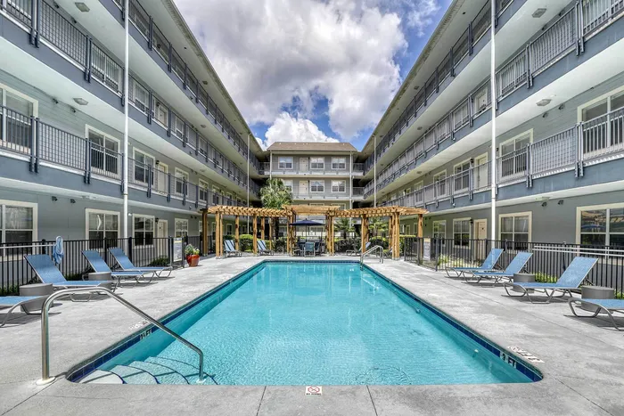 Inviting apartment complex showcasing a serene swimming pool surrounded by sleek lounge chairs, set against stylish multi-level balconies.
