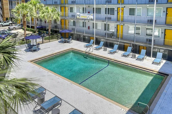 Inviting apartment courtyard featuring a sparkling swimming pool, surrounded by modern lounge chairs and vibrant yellow accents, perfect for relaxation and leisure.