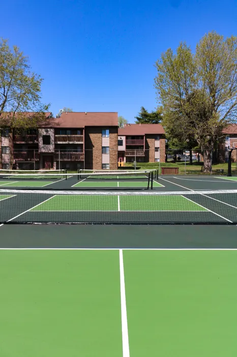 Close-up view of pickleball courts with vibrant green surfaces and nets, surrounded by trees and apartment buildings in a professionally managed community.