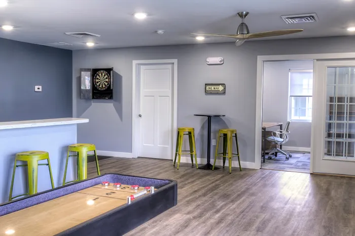 Lounge with shuffleboard and dart board &ndash; Modern resident lounge offering shuffleboard, a mounted dart board, and tall bar seating, creating a social atmosphere at The Field Apartments.