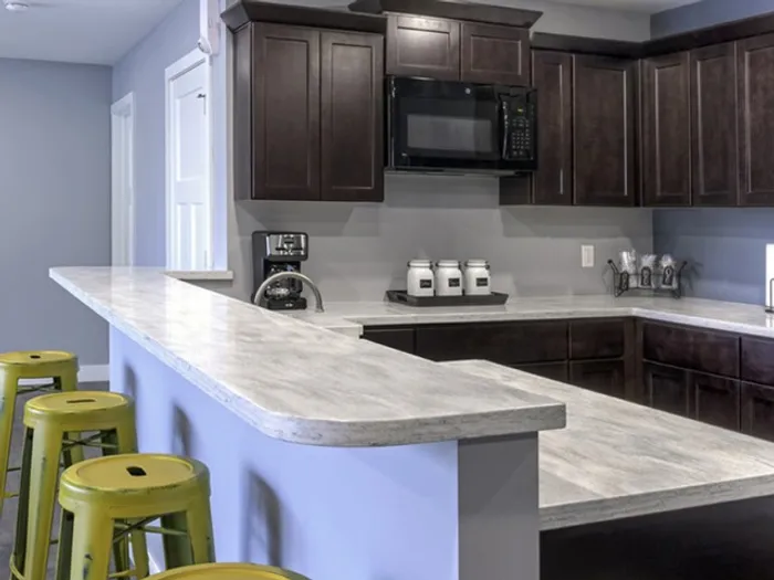 Resident clubhouse kitchen with bar seating &ndash; Stylish community kitchen inside the clubhouse, featuring dark wood cabinets, white marble-style countertops, and green metal bar stools at The Field Apartments in Springfield, Missouri.