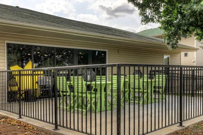 Fenced patio with outdoor seating &ndash; Secure outdoor dining area with a black metal fence and matching lime green tables and chairs located next to the clubhouse at The Field Apartments.