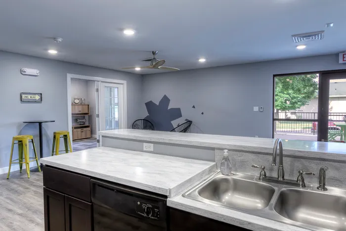 Clubhouse kitchen view from sink &ndash; View from behind the kitchen sink at The Field Apartments clubhouse, showing an open concept space with natural light, ceiling fan, and a wall mural accent.