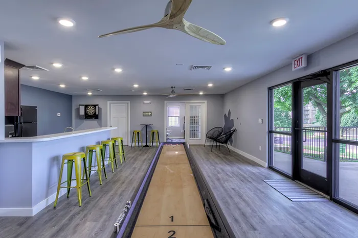 Shuffleboard table in clubhouse &ndash; Full-length shuffleboard table in a modern clubhouse space, with bar seating, lounge chairs, and access to outdoor areas at The Field Apartments.