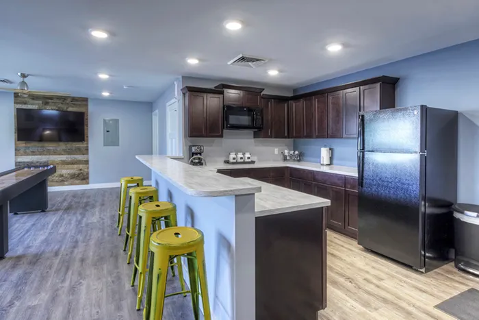 Community kitchen with seating &ndash; Modern community kitchen with dark cabinetry, light countertops, stainless steel appliances, and a row of lime green bar stools at The Field Apartments in Springfield.