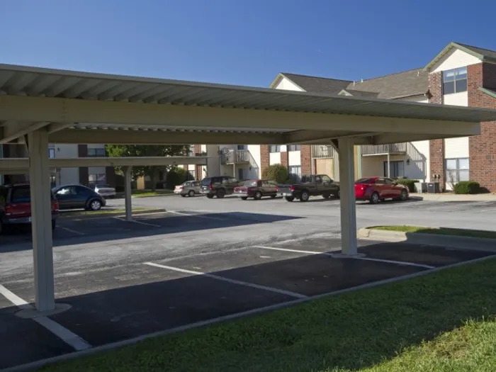 Multiple shaded parking spots available beneath a large covered carport, with apartment buildings in the background.