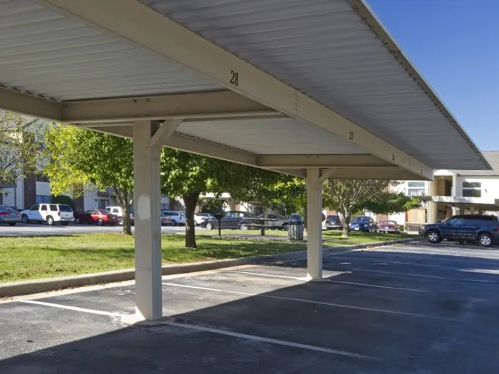 Well-maintained carport structure providing protected parking for residents, surrounded by mature trees and nearby apartments.