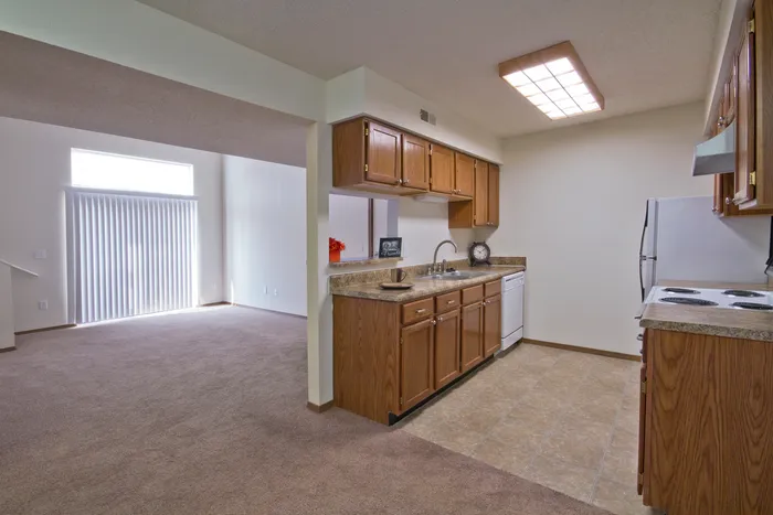 U-shaped kitchen with ample cabinet space opens to a carpeted dining and living area, offering an open-concept feel.