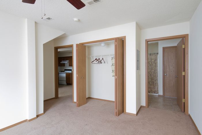 Spacious bedroom with two open closets, ceiling fan, and views into the bathroom and kitchen area.