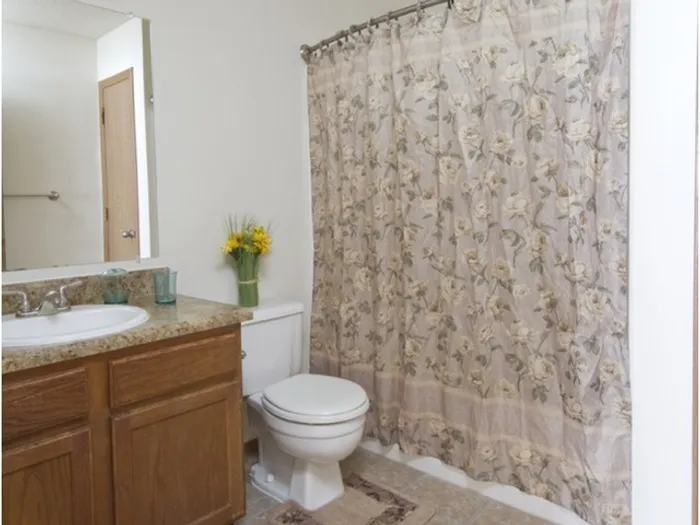 Bathroom featuring a wooden vanity, single-sink countertop, toilet, and shower with a floral curtain and accent d&eacute;cor.