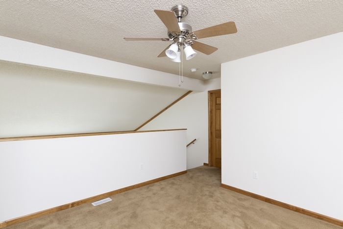 Upper-level loft area with partial wall overlooking the living room, complete with neutral carpet and ceiling fan for airflow.
