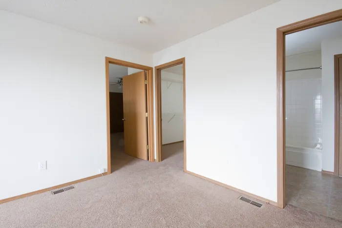 Neutral-toned room showing open doorway access to additional rooms and closets, featuring consistent trim and baseboards.
