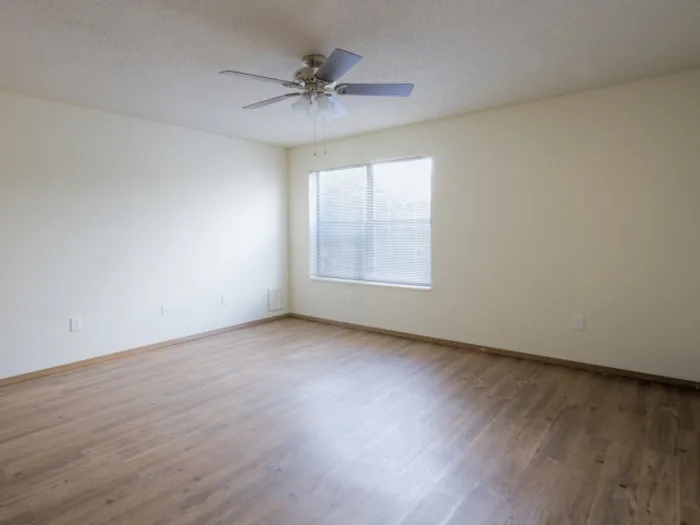 Bright, unfurnished bedroom with wood-look flooring, white walls, a large window, and a ceiling fan for year-round comfort.