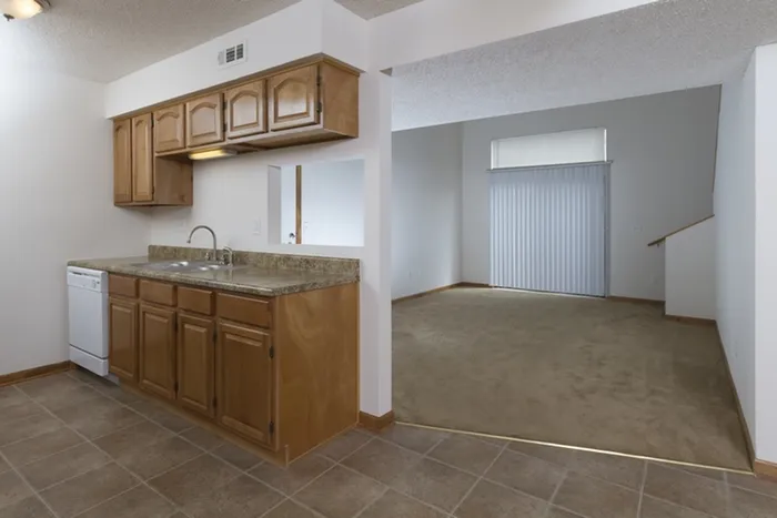 Open-concept kitchen with wood cabinetry and granite-look countertops, connected to a carpeted living space with sliding patio doors.