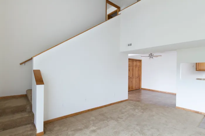 Spacious main living area featuring vaulted ceilings, neutral walls, and access to a lofted second level with wooden trim accents.