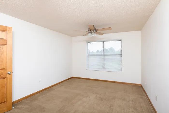 Unfurnished bedroom with neutral carpet, white walls, large window for natural light, and a ceiling fan for comfort.