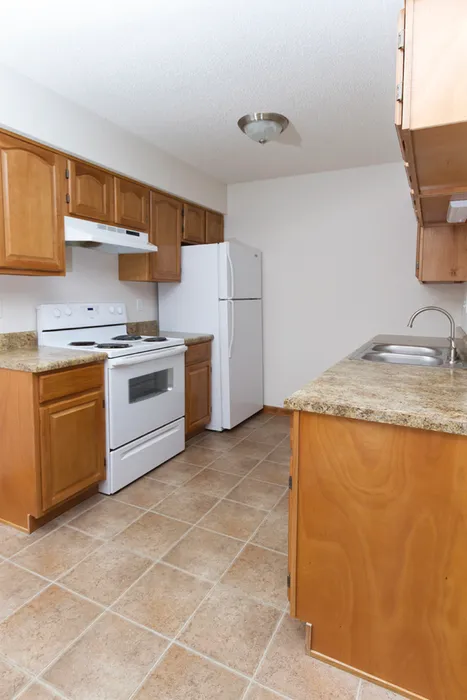 A kitchen featuring white appliances, including a gas stove, microwave oven, refrigerator, and sink. The cabinetry is also white, with countertops and a floor adding to the homey atmosphere of the room.