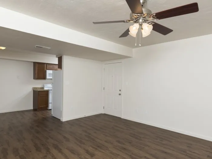 Open living space with hardwood-style flooring, a ceiling fan with light fixtures, and neutral walls, adjacent to a modern kitchen in a well-designed apartment unit.