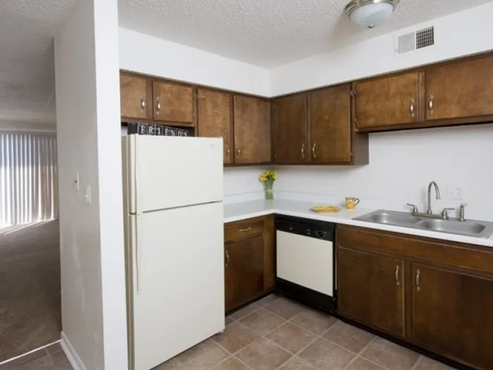 Compact kitchen with brown wooden cabinets, white appliances, and a small yellow flower vase on the counter. Clean, minimal, and functional space.