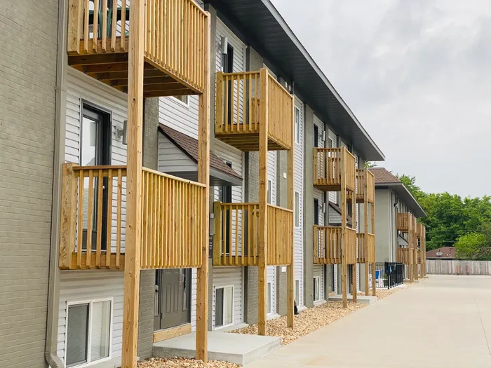 A row of modern two-story apartments with wooden balconies and gray siding on a cloudy day. The tone is neutral and organized.
