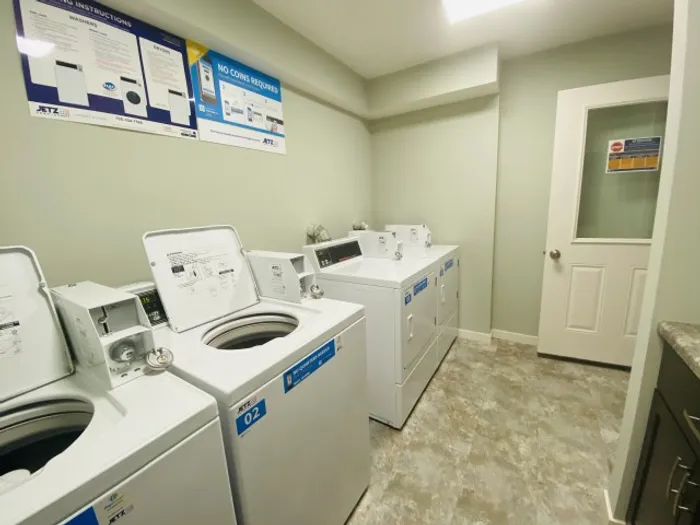 A clean laundry room with three white washing machines. Instruction posters hang on mint green walls. The room has a bright, organized appearance.