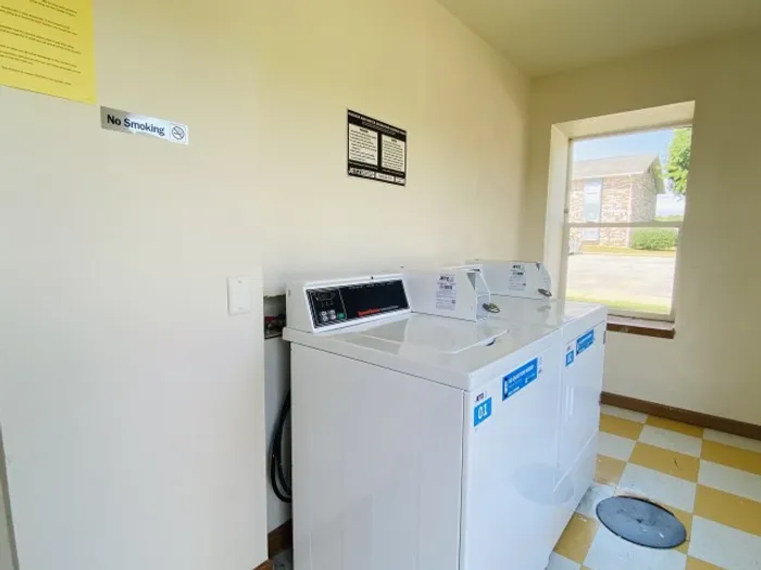 Laundry room with washer and dryer units, neutral walls, and window showing outside light.