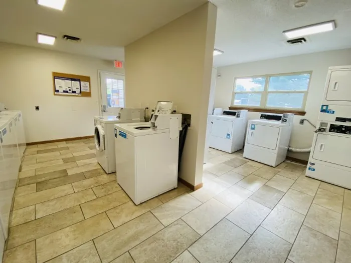 Clean laundry facility with washers and dryers spaced along tile floors, natural light streaming through large windows.