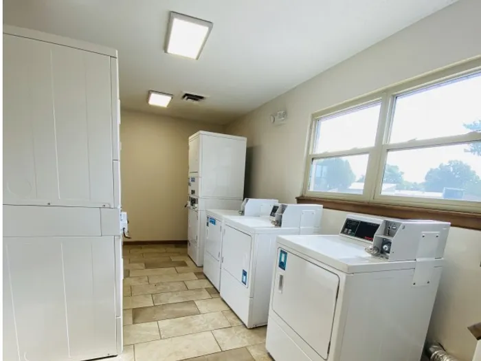 Functional laundry space with stacked dryers and cabinets for storage, illuminated by daylight from a nearby window.