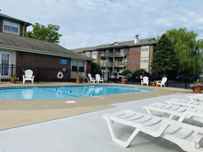 Outdoor swimming pool surrounded by white lounge chairs and brick apartment buildings, offering a relaxing amenity space for residents.
