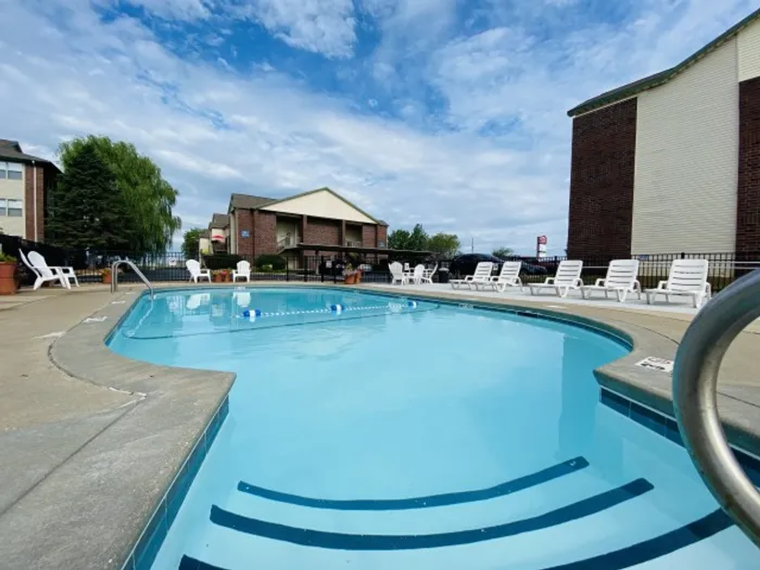 Large oval pool with gentle reflections of the sky, encircled by white lounge chairs and shaded trees, creating a calm atmosphere.