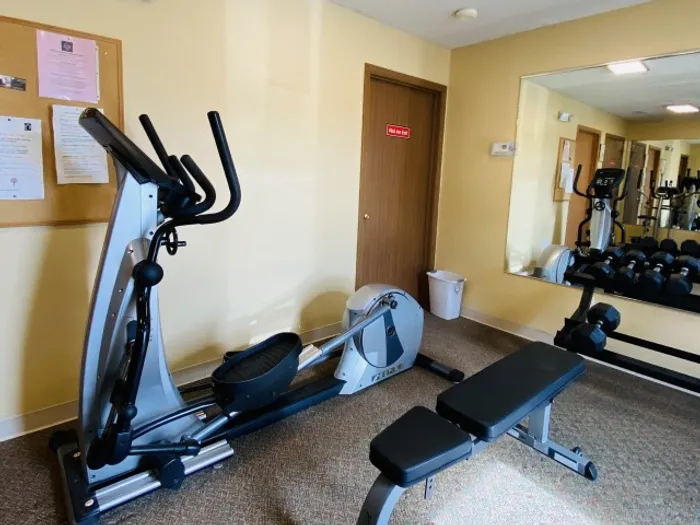 Smaller workout area within the fitness center featuring a bench press station, elliptical, and wall-mounted mirror for functional training.