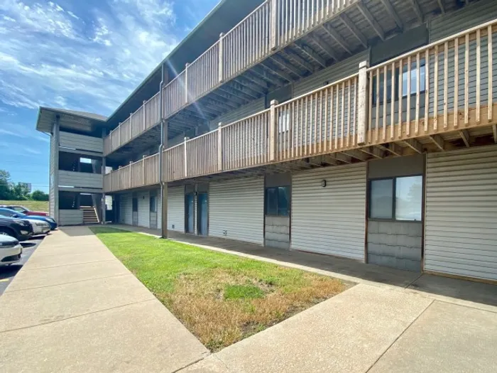 Outdoor view of a three-story apartment building with wood balconies and walkways surrounding a small grassy courtyard.