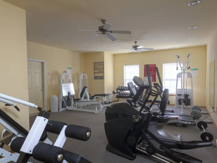 Fitness center at Plainview Park Apartments featuring treadmills, weight machines, and ceiling fans in a well-lit space.