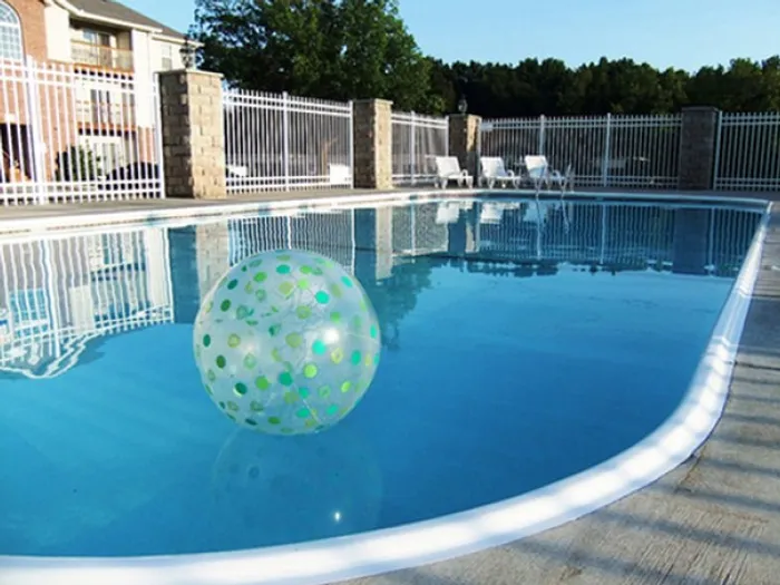 Curved outdoor pool with lounge chairs and a playful beach ball, surrounded by white fencing at Plainview Park Apartments.