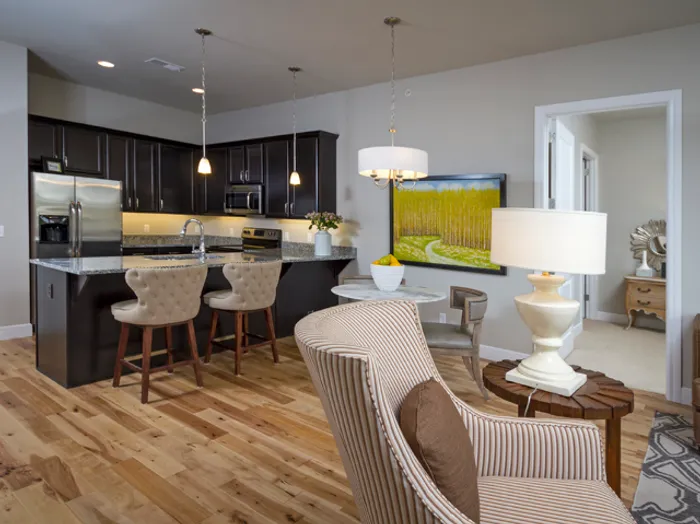 Spacious kitchen and dining area at Chesterfield Lofts in Springfield, MO, showcasing dark wood cabinetry, stainless steel appliances, and a granite countertop island with bar seating. The dining space features a round table with upholstered chairs and a decorative pendant light, creating a stylish and inviting atmosphere in this modern apartment home.