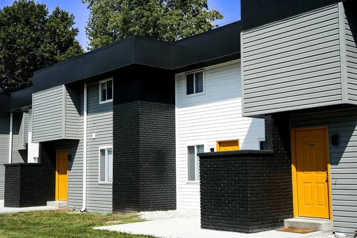 Renovated apartment building with gray and white siding, black brick accents, and multiple bright yellow front doors beneath a flat black roofline.