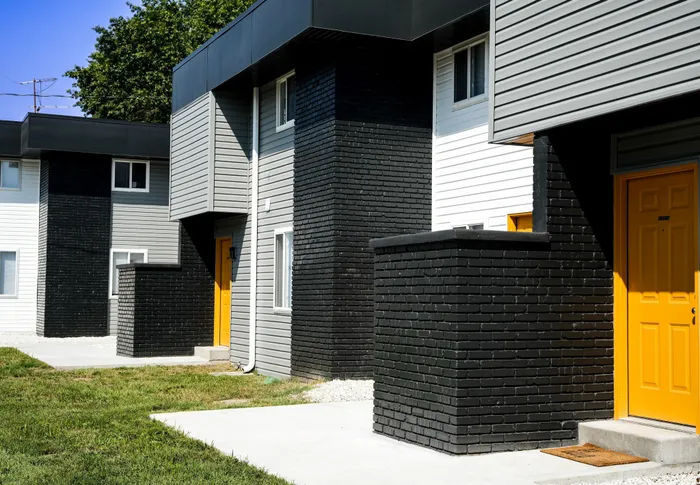 Close view of townhomes with black painted brick entrances and yellow doors. Siding in gray and white under modern black flat roofing.