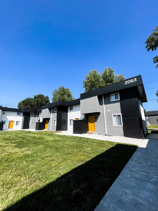 Wide view of a row of townhome-style apartment buildings with unit number 2063. Gray and white exteriors, black trim, and yellow front doors.