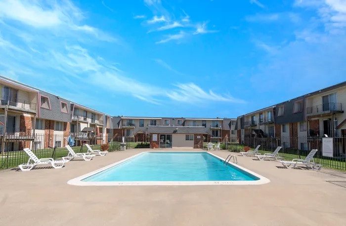 Large outdoor swimming pool surrounded by lounge chairs and two-story brick apartment buildings at Rosewood Village in Springfield, Missouri.
