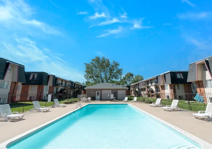 Bright blue swimming pool with lounge chairs and well-maintained two-story apartments in the background at Rosewood Village Apartments.
