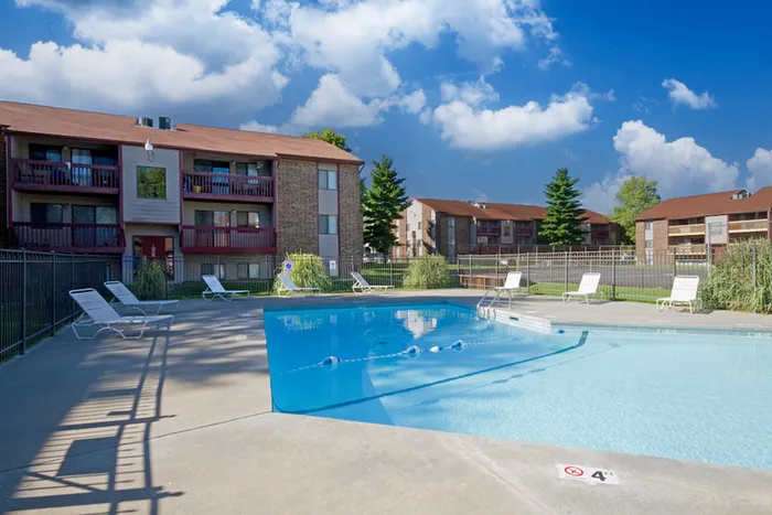 Outdoor swimming pool with clear water, surrounded by lounge chairs, secure fencing, and apartment buildings in the background, showcasing community amenities in a professionally managed property.
