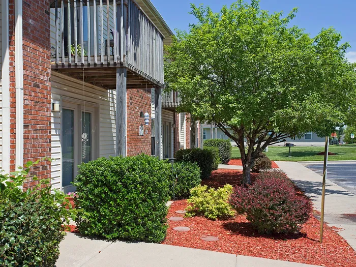 Well-maintained exterior of Huntley Ridge Apartments featuring red mulch landscaping, trimmed bushes, and mature trees near ground-level units with private patios.