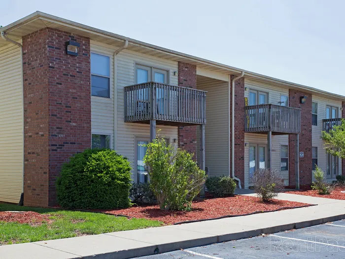 Exterior of a two-story apartment building at Huntley Ridge with small balconies, red mulch garden beds, and manicured bushes along the sidewalk.