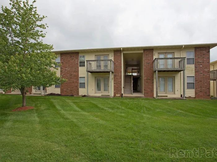 Wide grassy courtyard behind a Huntley Ridge Apartments building, showing symmetrical two-story units with private patios and balconies.