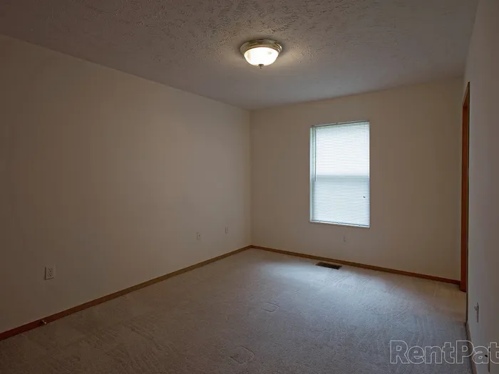 Spacious interior room at Huntley Ridge Apartments with neutral walls, carpet flooring, single window, and ceiling light&mdash;ideal for a living area or bedroom.
