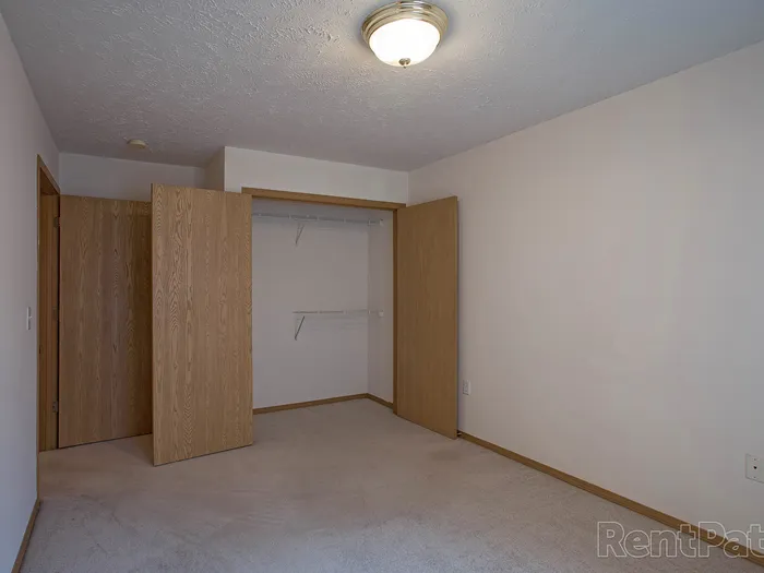 Carpeted bedroom at Huntley Ridge Apartments featuring neutral walls, ceiling light fixture, and an open double-door closet with shelving and hanging space.