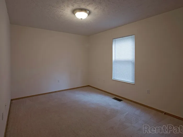 Unfurnished bedroom showcasing soft carpet, clean white walls, and a single window with blinds offering natural light.
