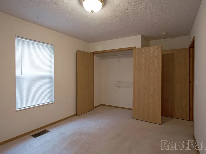 Bright bedroom with a large open closet, window with blinds, and beige carpet&mdash;ideal for personalized layout options.