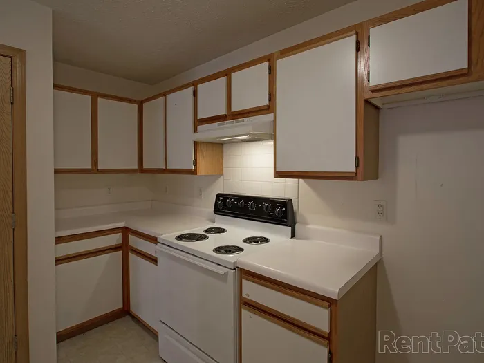 Galley-style kitchen featuring white cabinetry, electric stovetop, range hood, and refrigerator, with clean countertops and overhead storage.