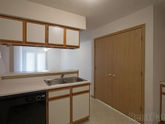 Double sink setup with white cabinetry and a view of closed pantry-style wooden doors, located in a bright kitchen nook with a partial pass-through.